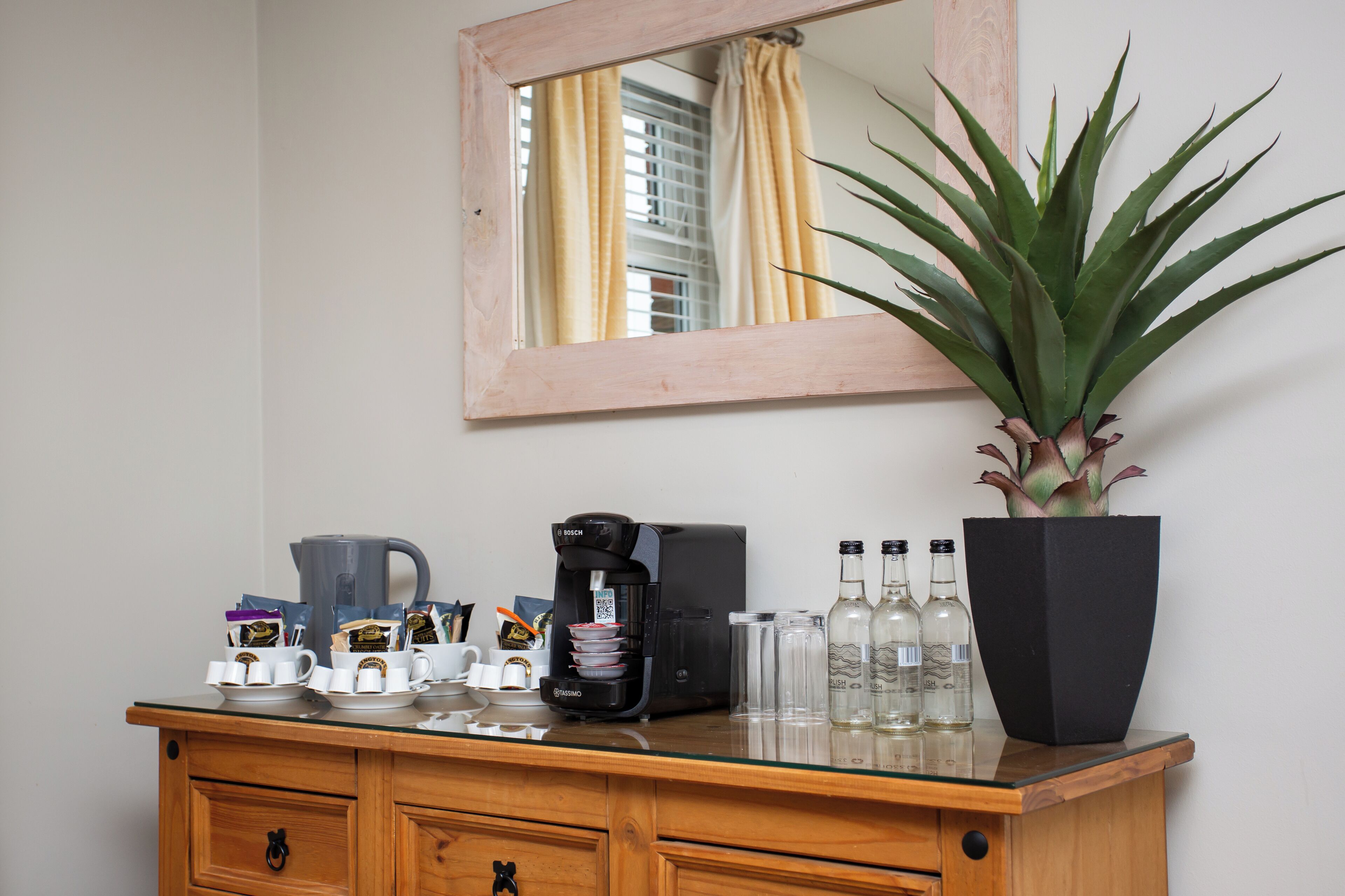 A wooden dresser with a coffee maker, cups, and bottles.