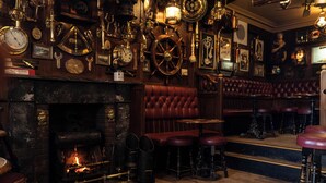 A bar with a fireplace, leather seating, and various clocks and decorative items on the walls. - The Olde Ship Inn (Seahouses)