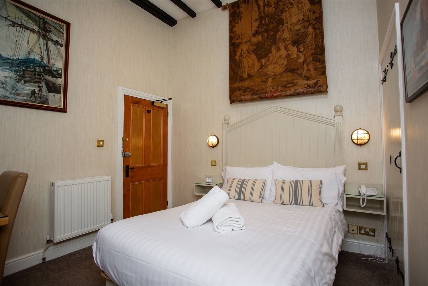 Una habitación de hotel con una cama, una puerta de madera, un cuadro y una lámpara fijada a la pared.