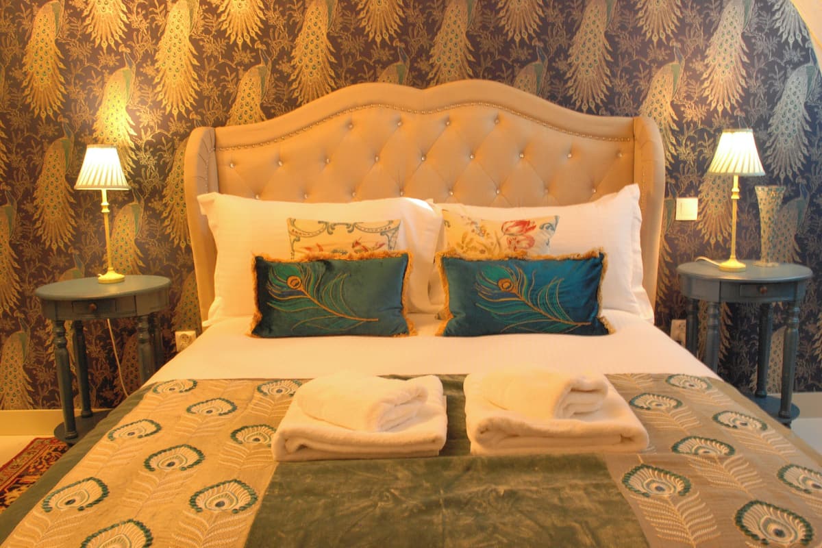Una cama bien hecha con dos almohadones decorativos, una toalla doblada y dos lámparas de noche en mesitas a juego.