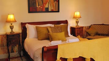 Una cama bien tendida con un edredón amarillo y varios almohadones, flanqueada por dos mesitas de noche con lámparas.