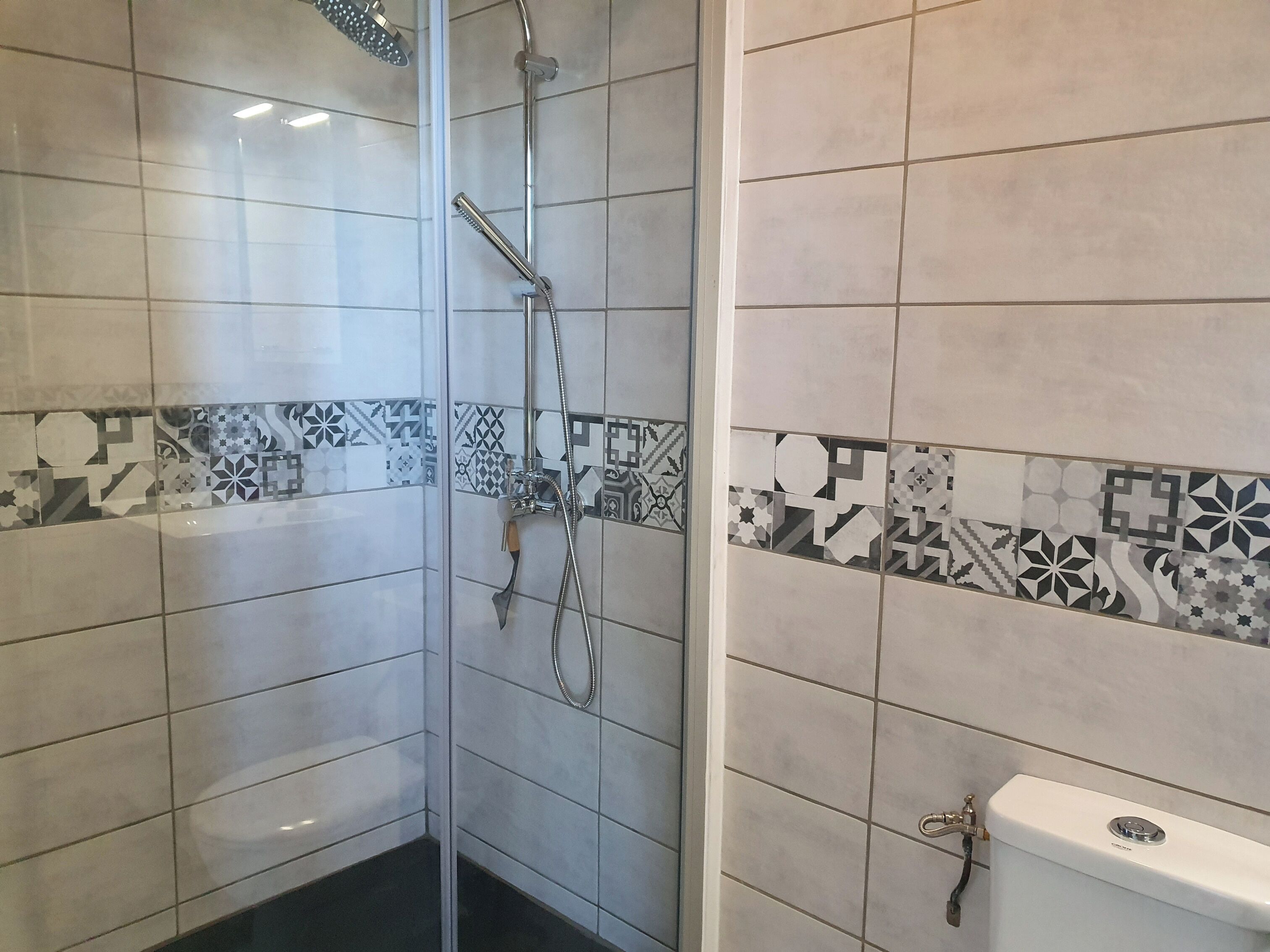 Un baño con ducha, inodoro y paredes de azulejos.