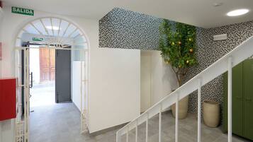 Un pasillo con una puerta blanca que dice "SALIDA", un papel tapiz decorativo, una escalera y una planta con frutos amarillos.