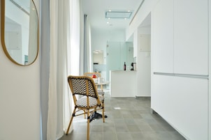 Una cocina moderna con armarios blancos, un comedor con una silla y una mesa, y un espejo grande en la pared.