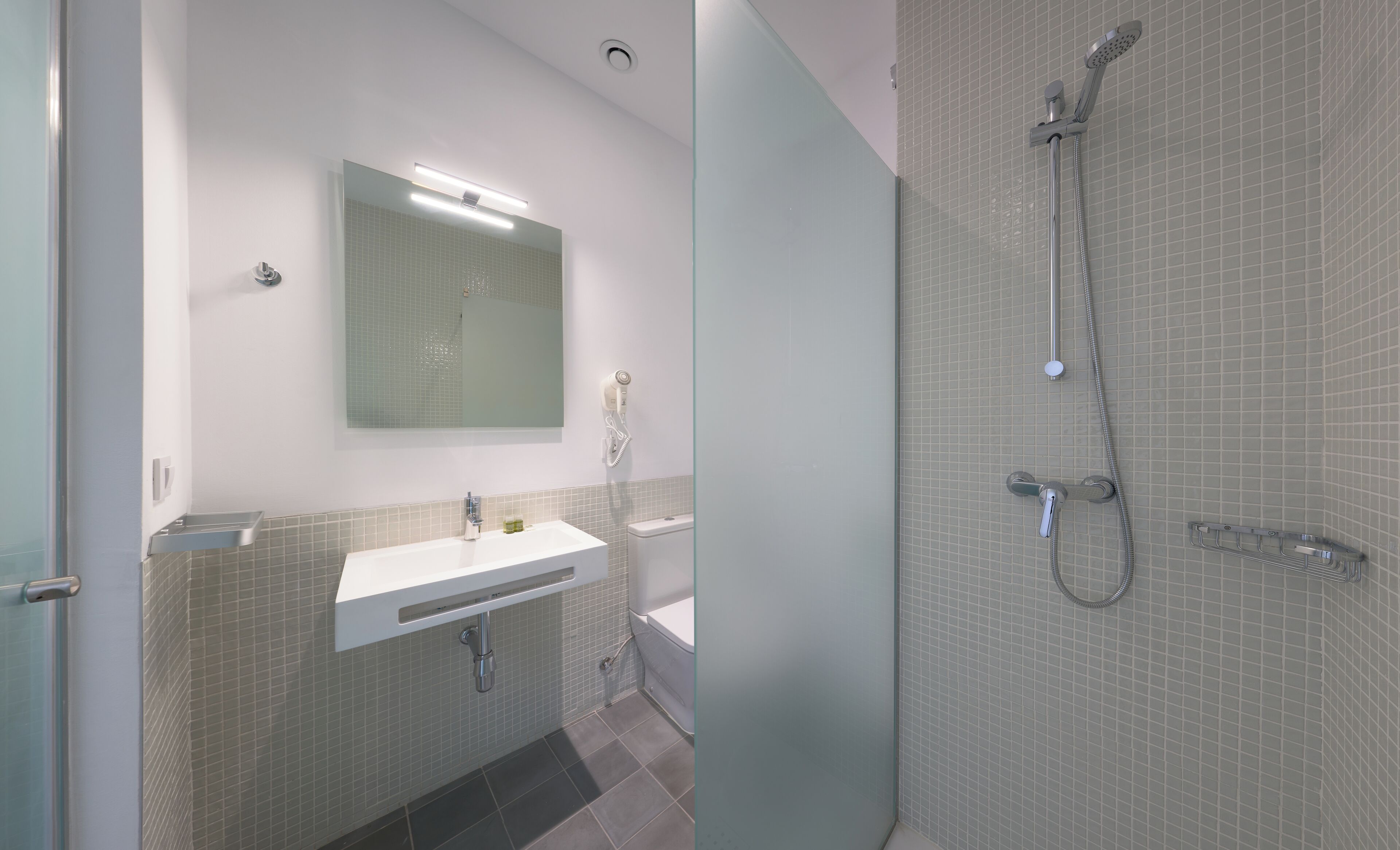 Une salle de bain moderne avec un lavabo blanc, un miroir, une douchette à main et des toilettes.
