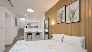 Une chambre d’hôtel moderne avec un grand lit, un bureau et, au fond, une petite cuisine.