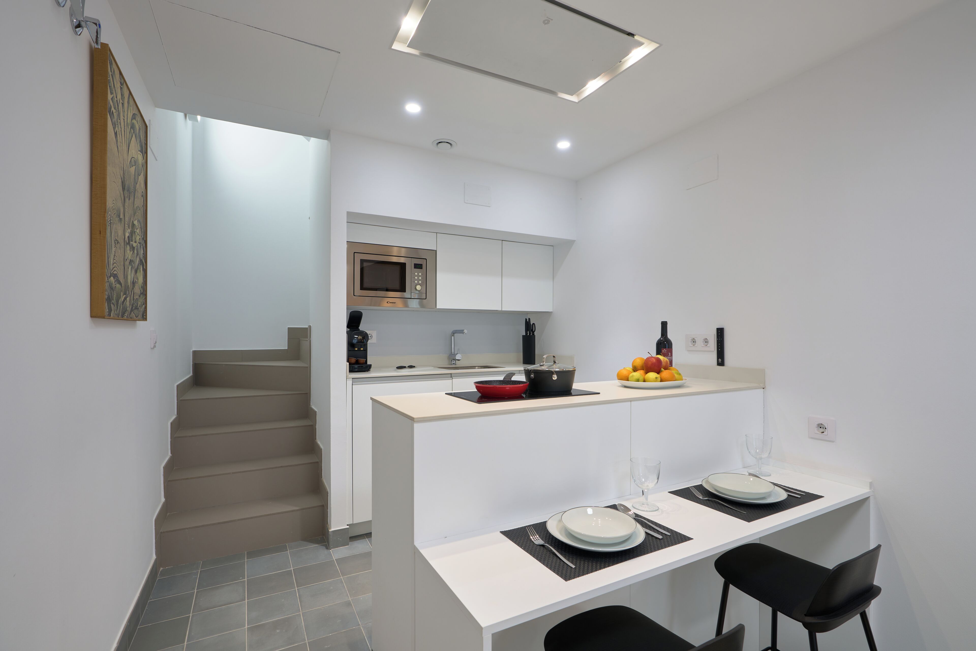 Une cuisine moderne avec des meubles blancs, un four à micro-ondes et un coin repas avec une table dressée pour deux personnes.