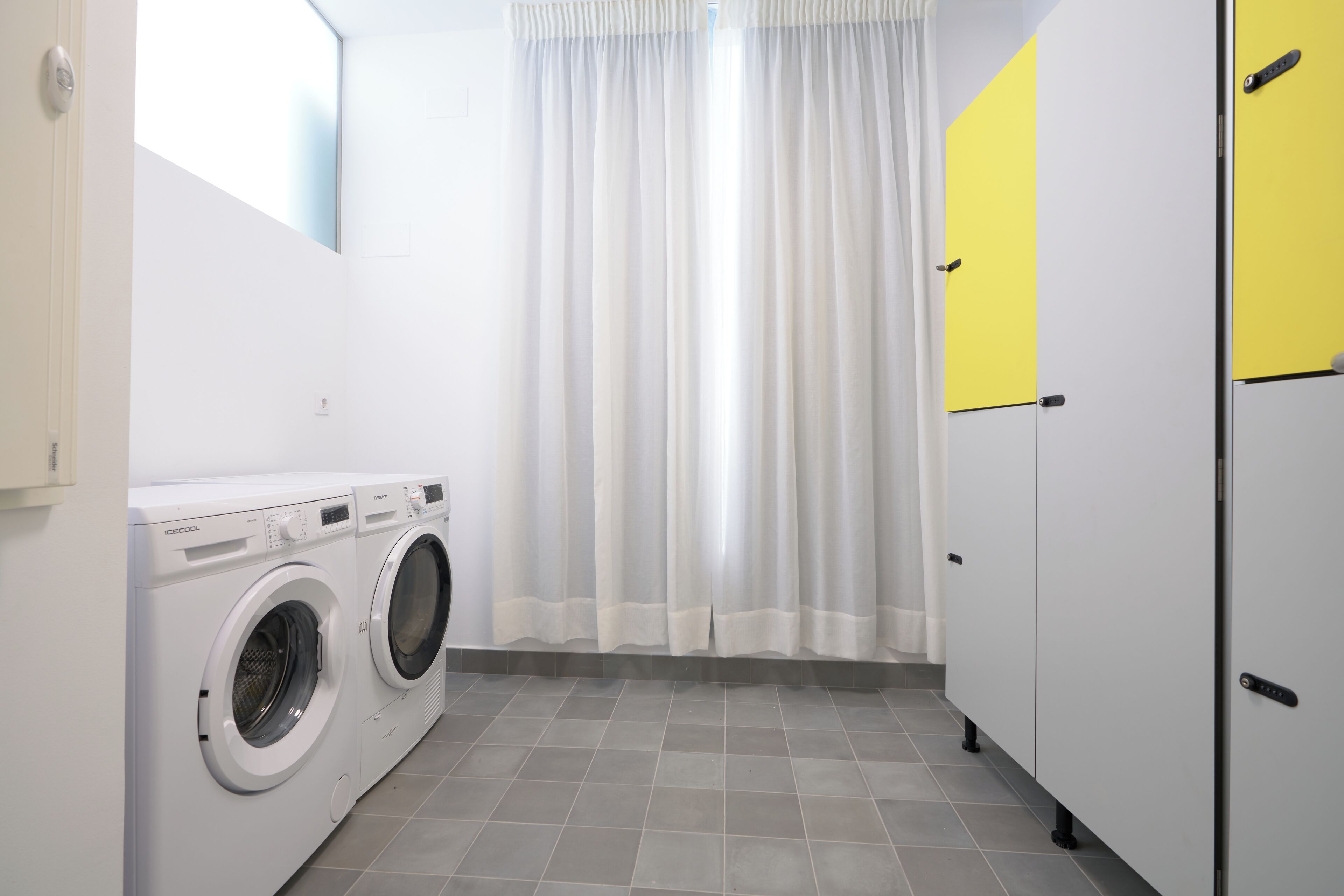 Une buanderie équipée de deux machines à laver à chargement frontal, d’un rideau blanc et d’une porte jaune.