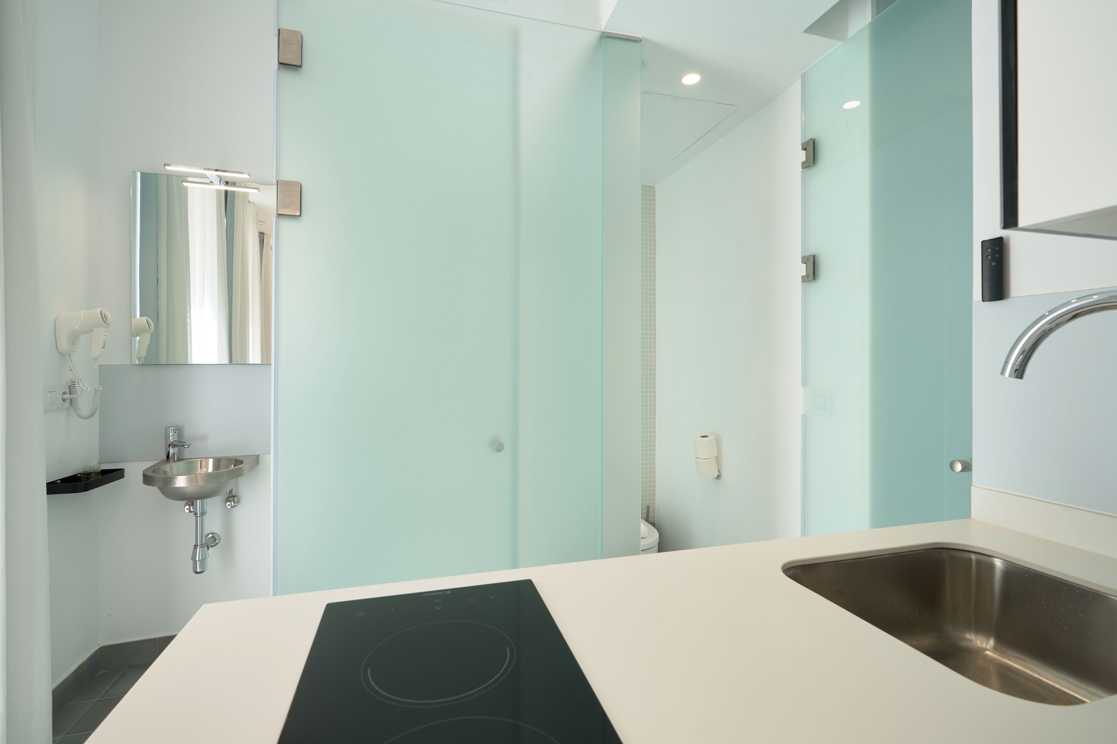 Un baño moderno con encimera blanca, lavabo de acero inoxidable y cabina de ducha con mampara de vidrio.