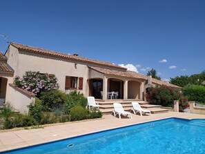 Une maison avec une piscine, une terrasse dotée de chaises longues et un jardin parsemé de fleurs roses.