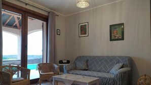 Ett vardagsrum med en soffa, två fåtöljer i rotting, ett soffbord och en taklampa.