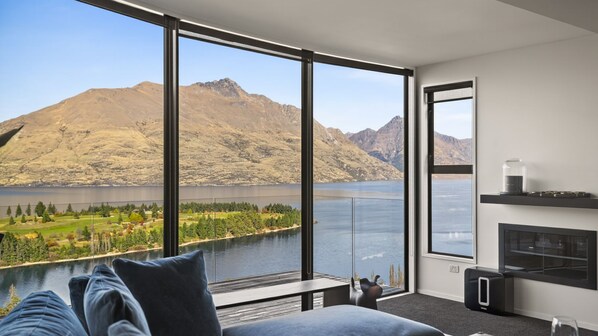Une chambre moderne avec de grandes fenêtres donnant sur un lac et des montagnes.