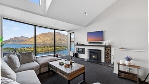 Un salon moderne comprenant un canapé, une table basse, une cheminée, un téléviseur et offrant une vue magnifique sur les montagnes et le lac.