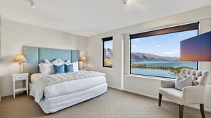 Une chambre à coucher avec un grand lit, deux tables de chevet, une chaise et une vue sur un lac et des montagnes.