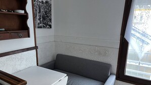 A corner room with a white desk, a grey sofa, a wooden shelf, and a black and white cityscape photo on the wall.