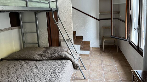 A dormitory room with bunk beds, a staircase, and a window.