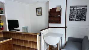 A compact living space with a kitchenette, a small white table, a gray sofa, and a framed cityscape picture on the wall.