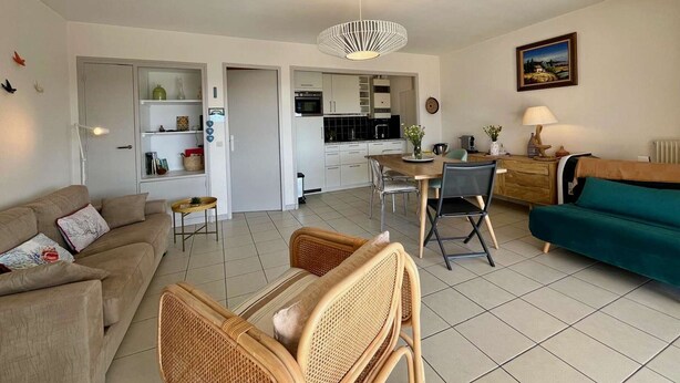 Ein Wohnzimmer mit Sofa, Sesseln, einem Esstisch und einer Küche im Hintergrund.