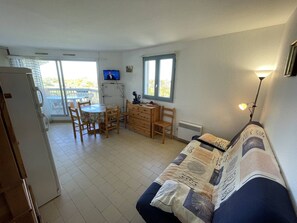 Un espace de vie compact comprenant un coin cuisine, un espace repas, un canapé et un téléviseur.
