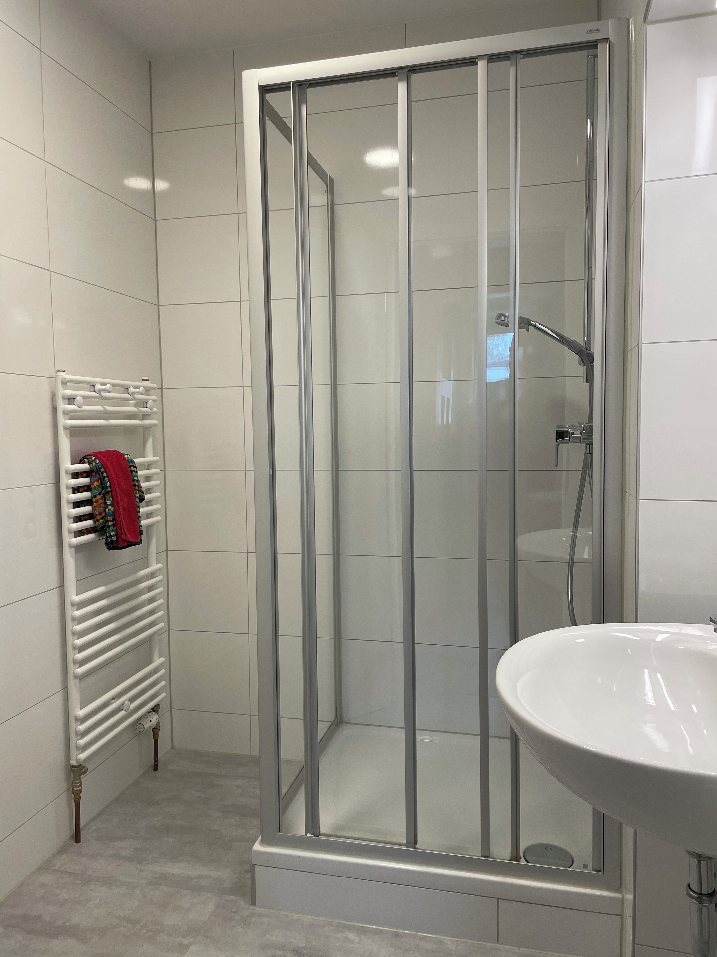 A modern bathroom with a glass-enclosed shower, a white sink, and a towel rack with colorful towels.