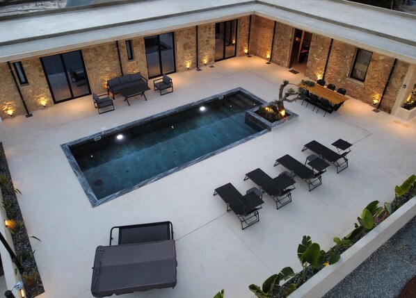 An outdoor pool area with a rectangular pool, lounge chairs, and a seating area with tables and chairs.