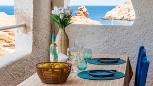 Tavolo imbandito per due con vista mare attraverso una finestra ad arco, un vaso con fiori e un cesto di limoni.