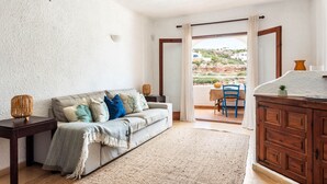 Un soggiorno con un divano, un armadio in legno, una ventola a soffitto e vista all'esterno tramite una porta in vetro.