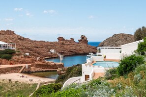A coastal resort with a pool, rocky cliffs, and a clear view of the sea.