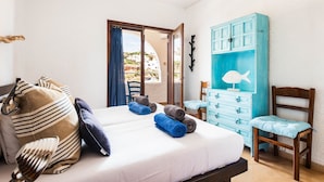 Una camera da letto con un letto, una sedia in legno, un comò blu e vista all'esterno.
