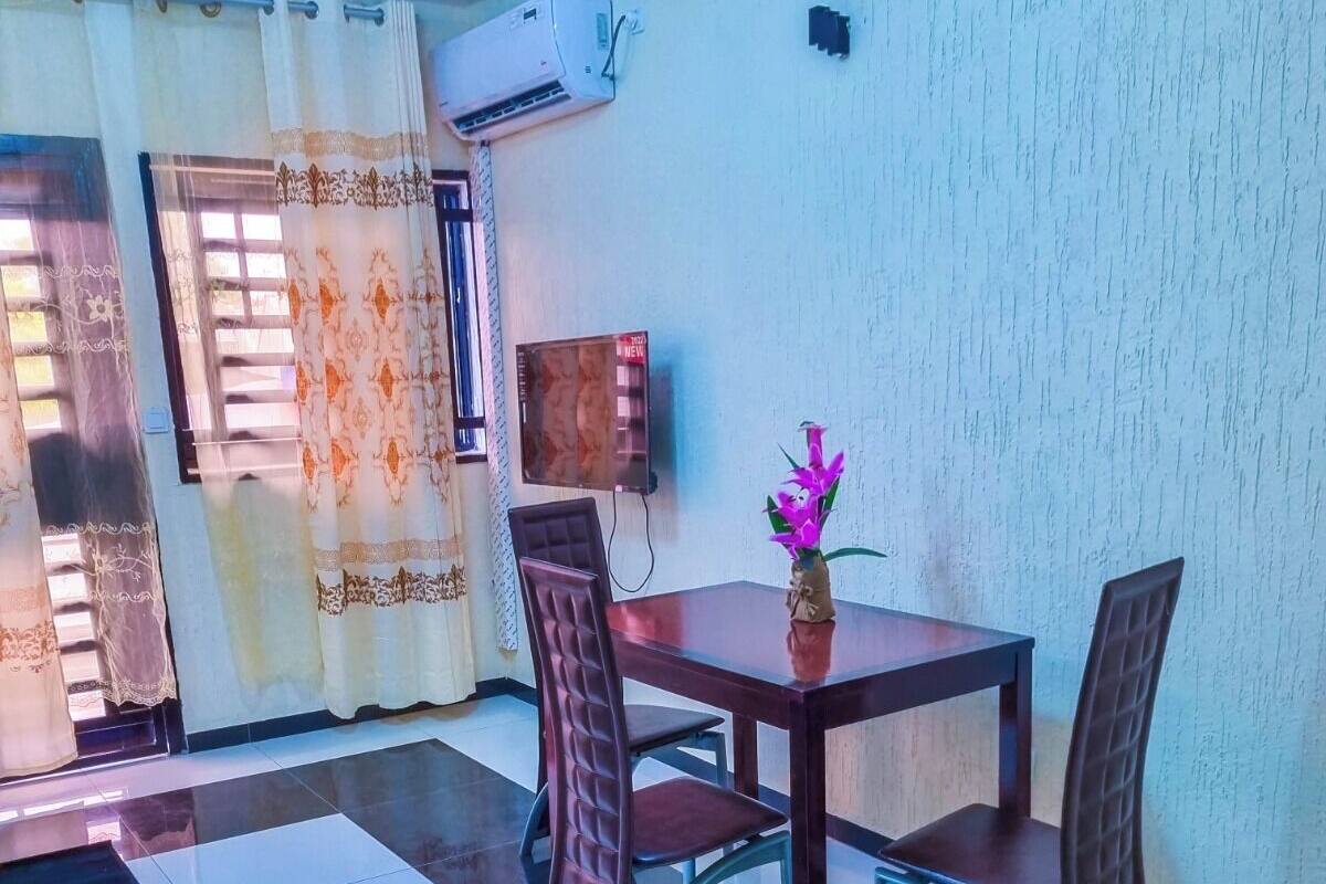 A dining area with a table and chairs, a small vase with flowers, and an air conditioning unit on the wall.
