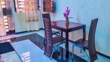 A dining area with a table and chairs, a small vase with flowers, and an air conditioning unit on the wall.