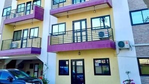A multi-story building with balconies, a car parked in front, and a potted plant. - NN GUEST HOUSE  (Bonaberi)