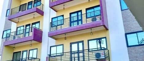 Un edificio de varios pisos con balcones, un coche estacionado al frente y una planta en maceta.