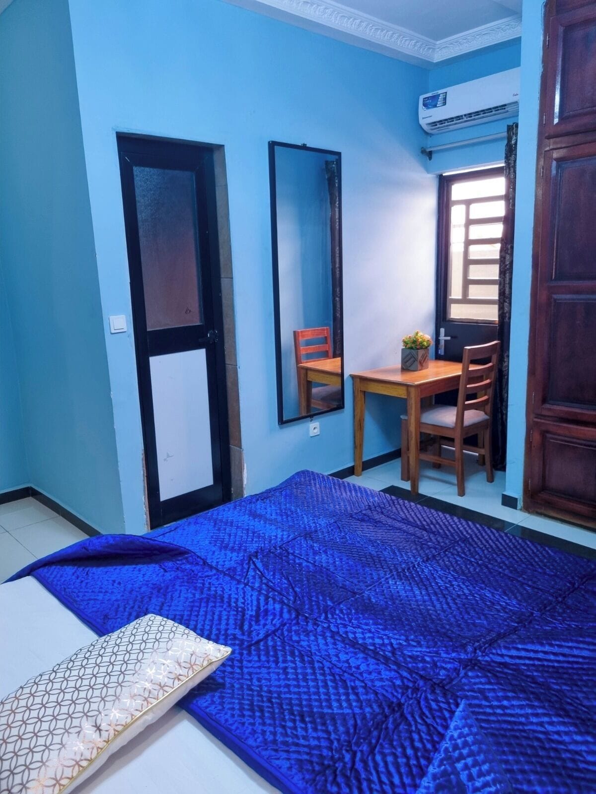A room with a bed, a desk, a chair, and a large mirror.