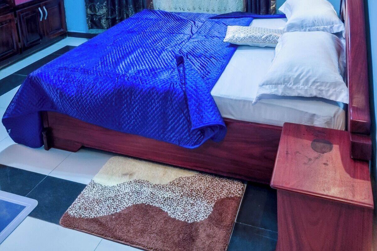A bedroom with a bed, a wooden nightstand, a television, and a window with patterned curtains.