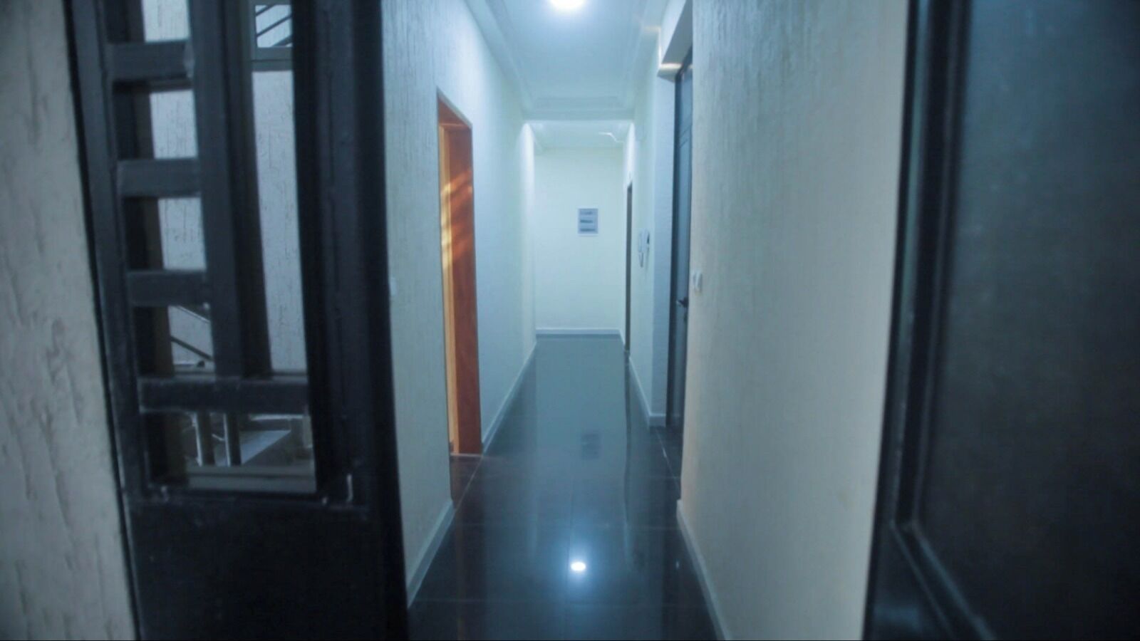 Un pasillo estrecho y tenuemente iluminado con una puerta de madera a la izquierda y una puerta blanca al final.