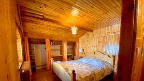 A wooden-paneled bedroom with a bed, a nightstand, a lamp, and a built-in wardrobe. - Chalet 12 Personne - Seul au Monde (Vars)