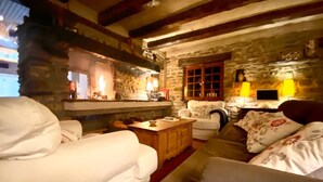 A cozy living room with stone walls, a fireplace, and a television. There are white sofas and a wooden coffee table. - Chalet 12 Personne - Seul au Monde (Vars)