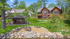 A large, multi-story log cabin with a stone fireplace, surrounded by a well-maintained lawn and a pond. - NEW! Cross Lake's Finest! (Crosslake)