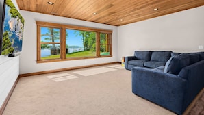 A modern living room with a large window, wooden ceiling, and a blue sofa. - NEW! Cross Lake's Finest! (Crosslake)