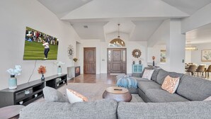 A modern living room with a large grey sectional sofa, a flat-screen TV mounted on the wall, and a dining area in the background. - Serene Retreat - Heated Pool, Spa, Sauna, Grass Pickleball (Sedona)