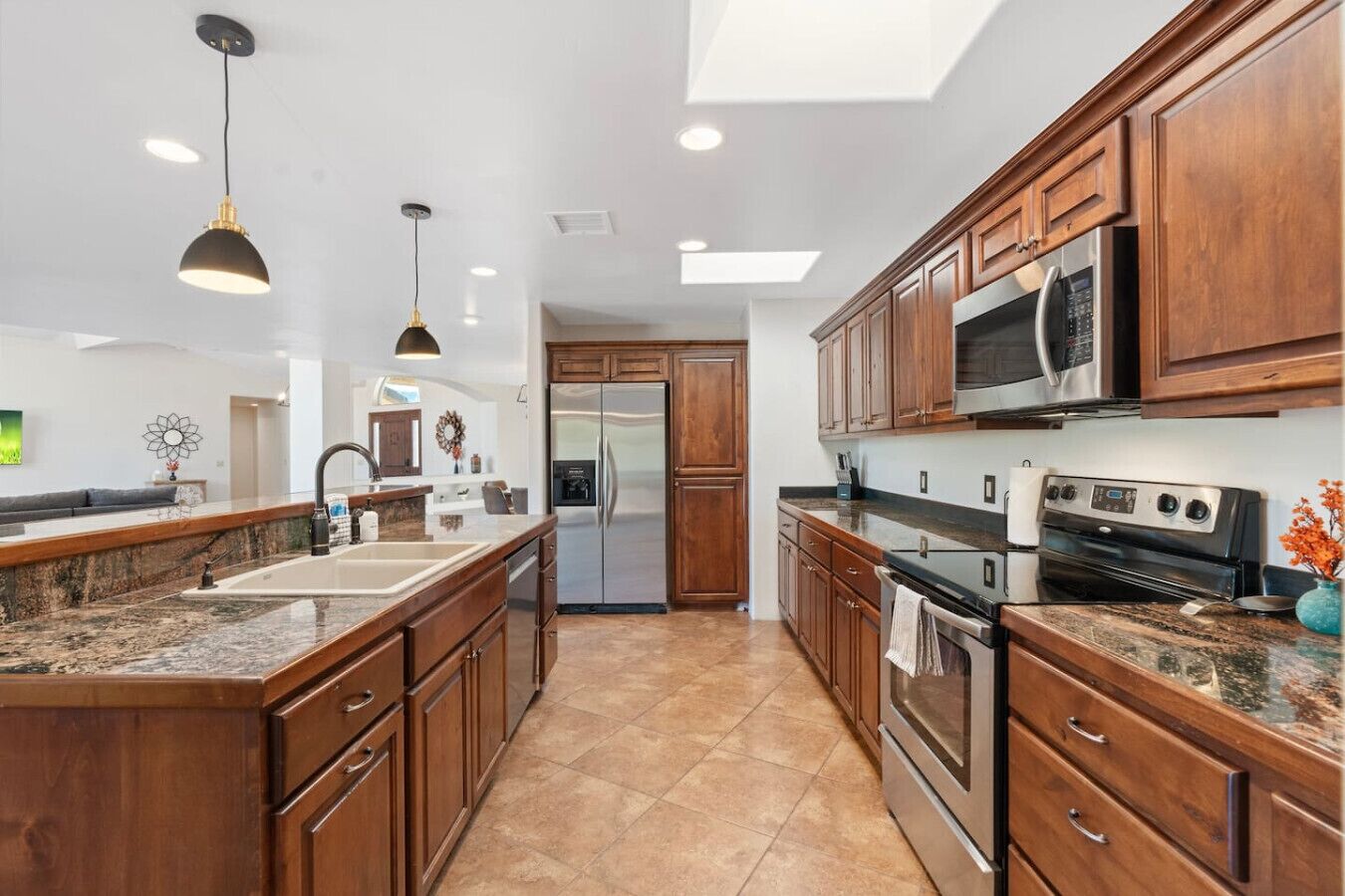 A modern kitchen with wooden cabinets, stainless steel appliances, granite countertops, and pendant lighting.