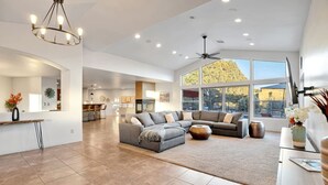 A spacious living room with a large sectional sofa, a dining area with a bar, and large windows offering a view of the outdoors. - Serene Retreat - Heated Pool, Spa, Sauna, Grass Pickleball (Sedona)
