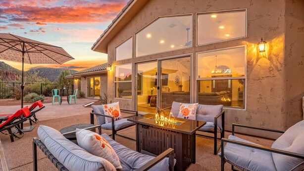 An outdoor patio with a fire feature, seating, and a view of the interior through large windows. - Serene Retreat - Heated Pool, Spa, Sauna, Grass Pickleball (Sedona)