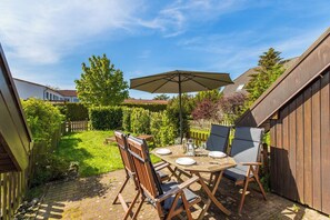 Une terrasse avec une table en bois, quatre chaises et un grand parasol.