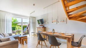 Un espace repas moderne avec une table en bois, des chaises noires et un téléviseur placé au-dessus d’une cheminée en pierre.