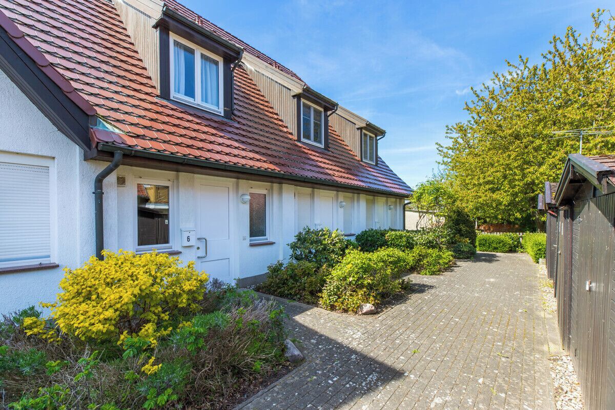 Een rij witte huizen met rode daken, een verharde oprit en groene struiken.