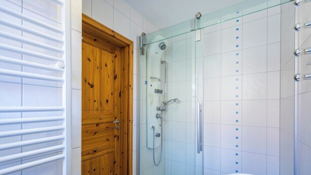 A bathroom with a glass-enclosed shower, a wooden door, and a white sink.
