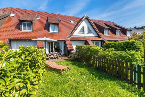 Une maison à deux étages avec un toit rouge, une cour arrière clôturée et une terrasse en bois.