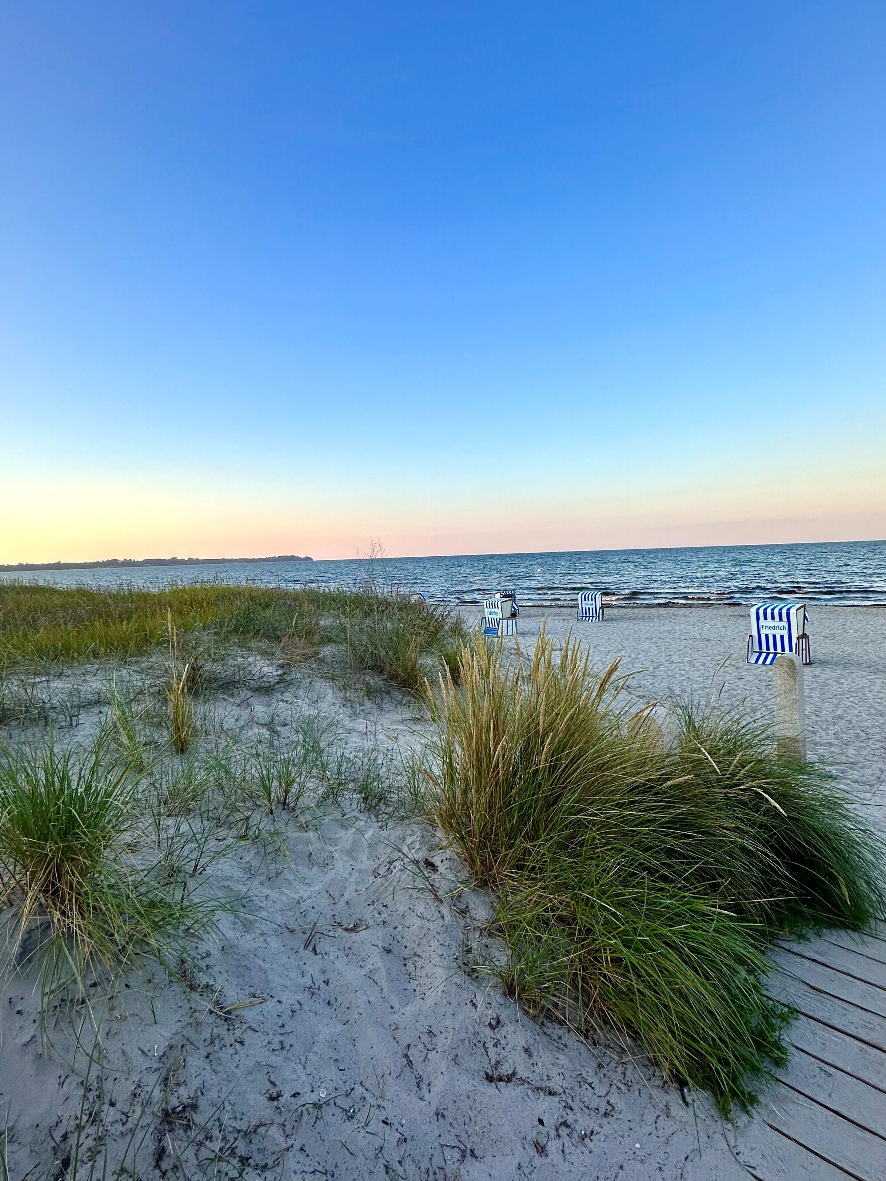 Ein Strand mit einer Holzpromenade, die zu gestreiften Liegestühlen führt.
